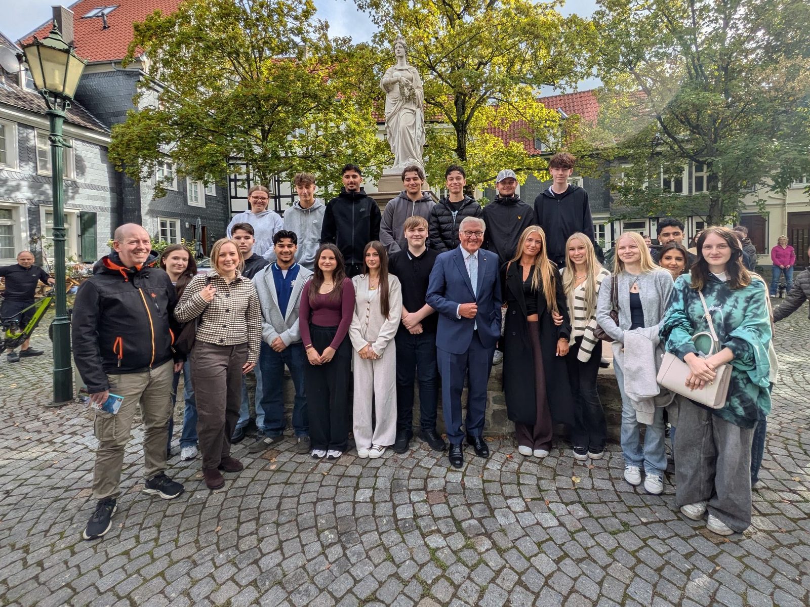 Gruppenfoto der Klasse HW 263 mit Bundespräsident Frank-Walter Steinmeier in der Mitte, dazu Lehrkraft und Schulleitung, vor einem Brunnen mit Frauenstatue zwischen Fachwerk- und Schieferhäusern in der Hattinger Altstadt