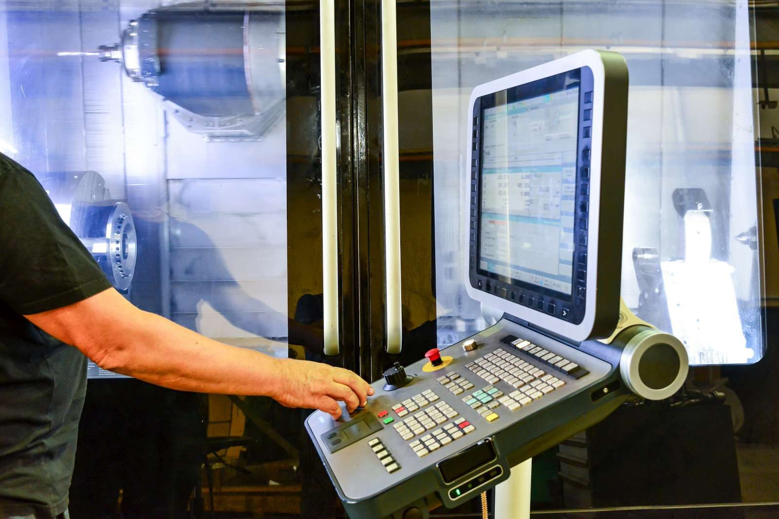 Eine Hand bedient das Steuerpult einer Werkzeugmaschine